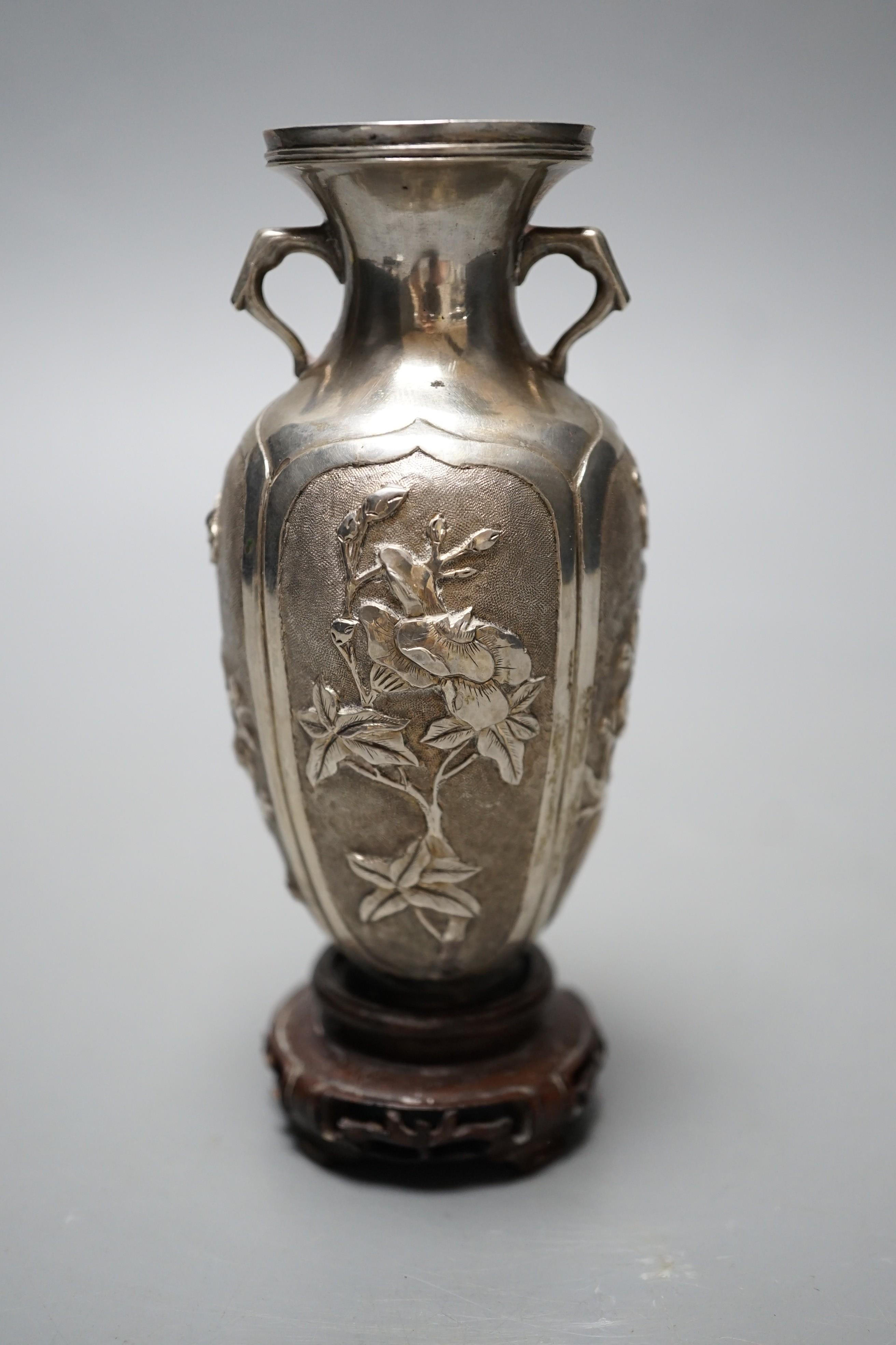 A late 19th/early 20th century Chinese Export white metal two handled vase, decorated with bamboo, peonies and prunus, on hardwood stand with white metal wing nut signed Zee Wo, vase 12cm.